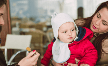 baby in red coat sitting being spoon-fed