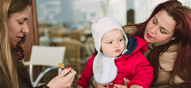 baby in red coat sitting being spoon-fed