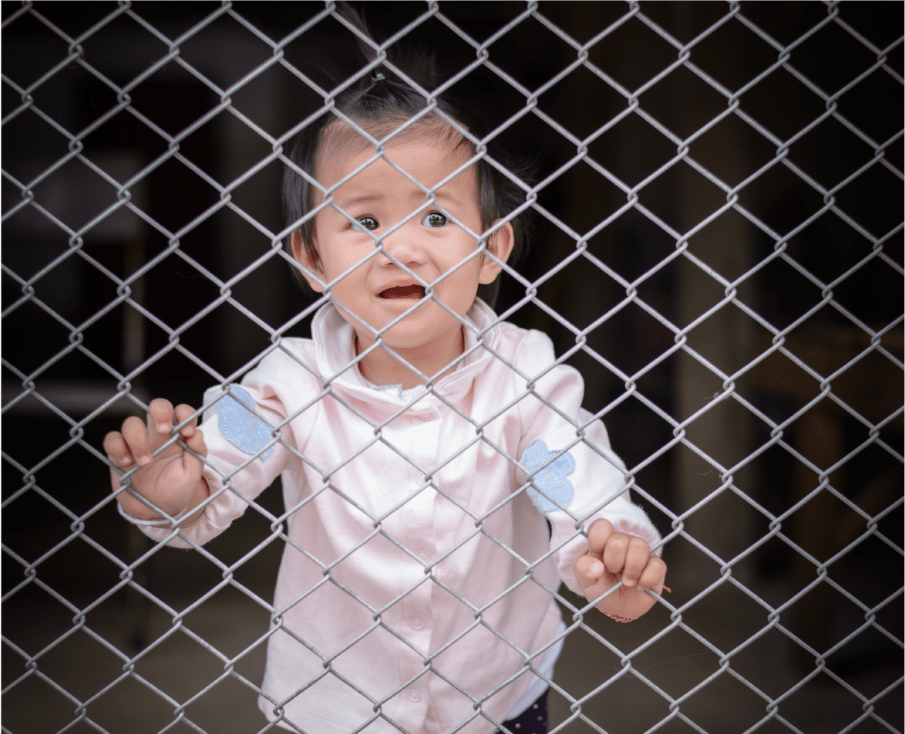 toddler standing behind fence gate crying