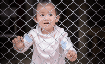 toddler standing behind fence gate crying