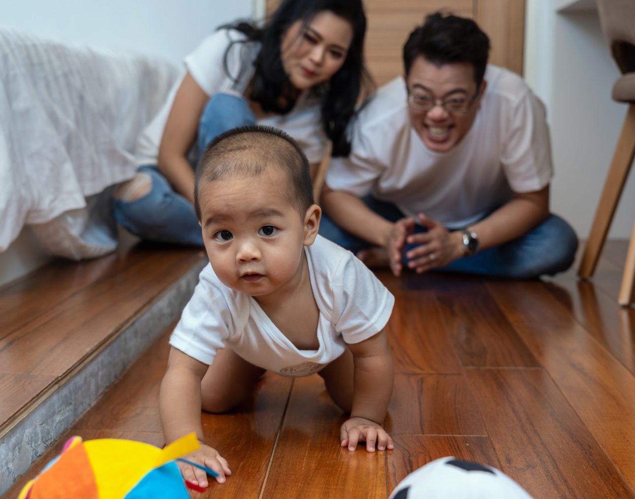 a baby crawling with parents smiling