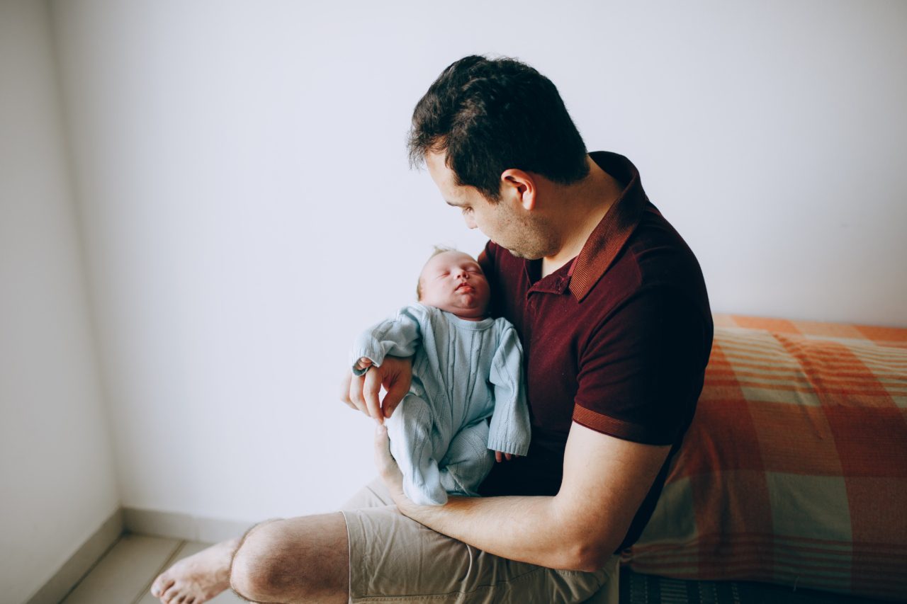 father wearing maroon holds newborn