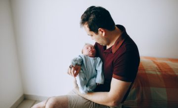 father wearing maroon holds newborn