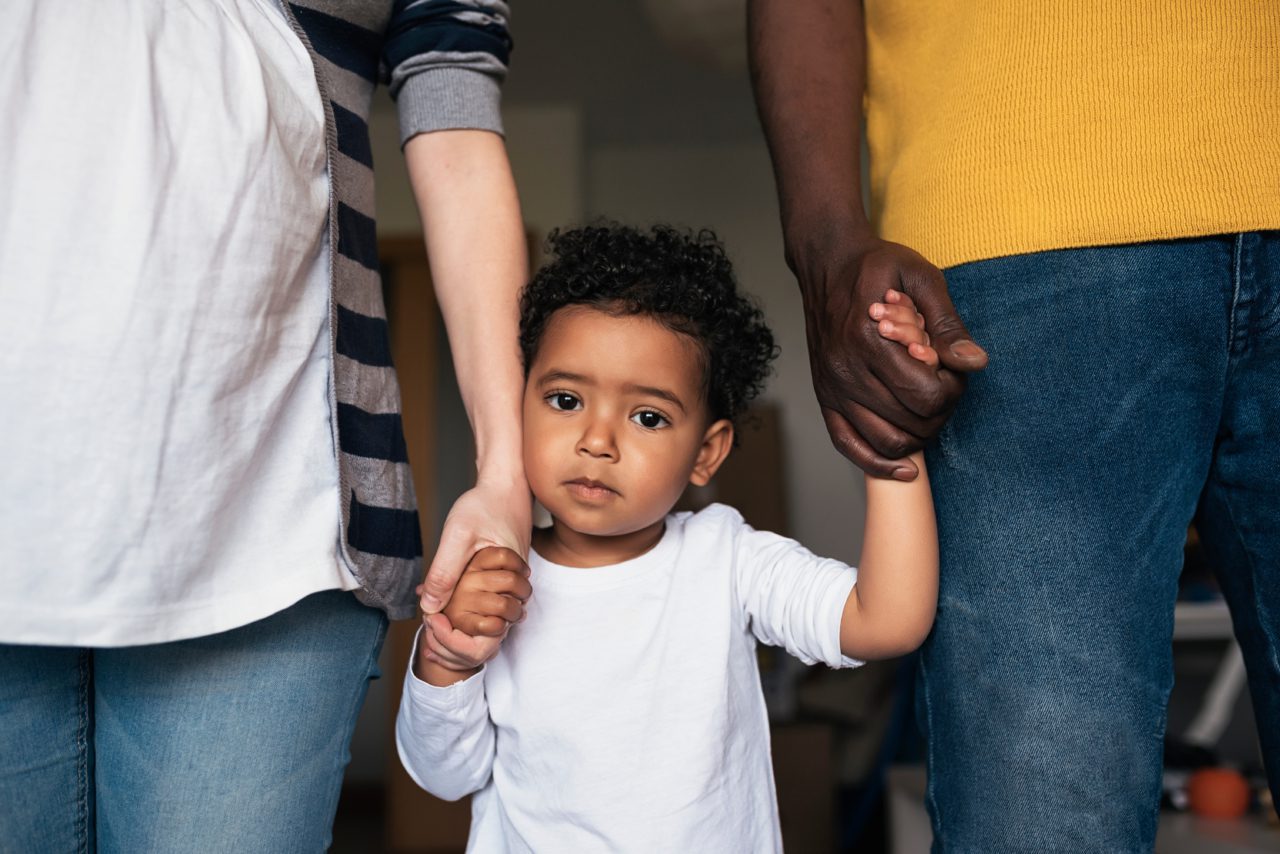 A sad child standing in between parents holding their hands