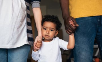 A sad child standing in between parents holding their hands