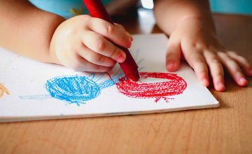 A child coloring a red and blue circle with crayon