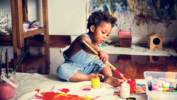 Toddler sitting on the floor dipping paintbrush in paint and making a picture