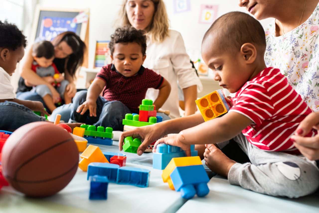 Toddlers playing with toys with caregivers nearby.