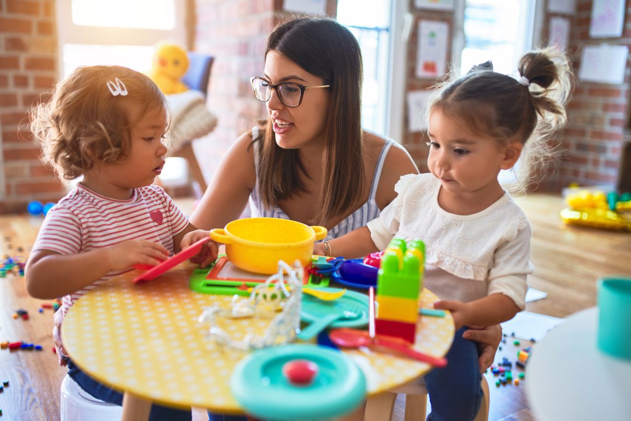 A teacher helps two small girls at a table in classroom