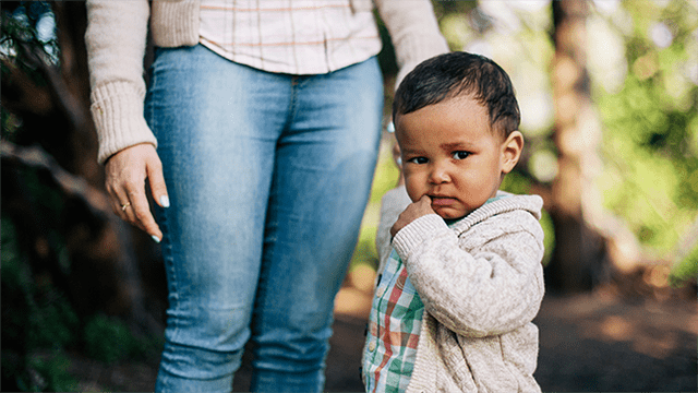 Young child stands next to adult caretaker outside