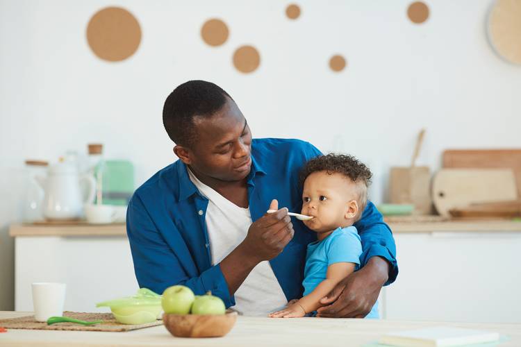 A man feeds a little boy in the kitchen