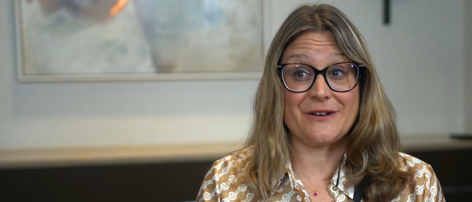 woman with glasses and long blonde hair talking to camera