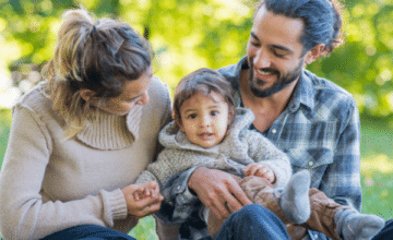 A family sits together outside. Mother, Father and Toddler.