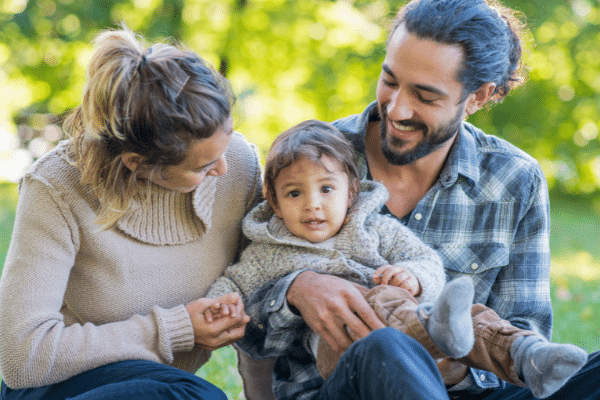 A family sits together outside. Mother, Father and Toddler.