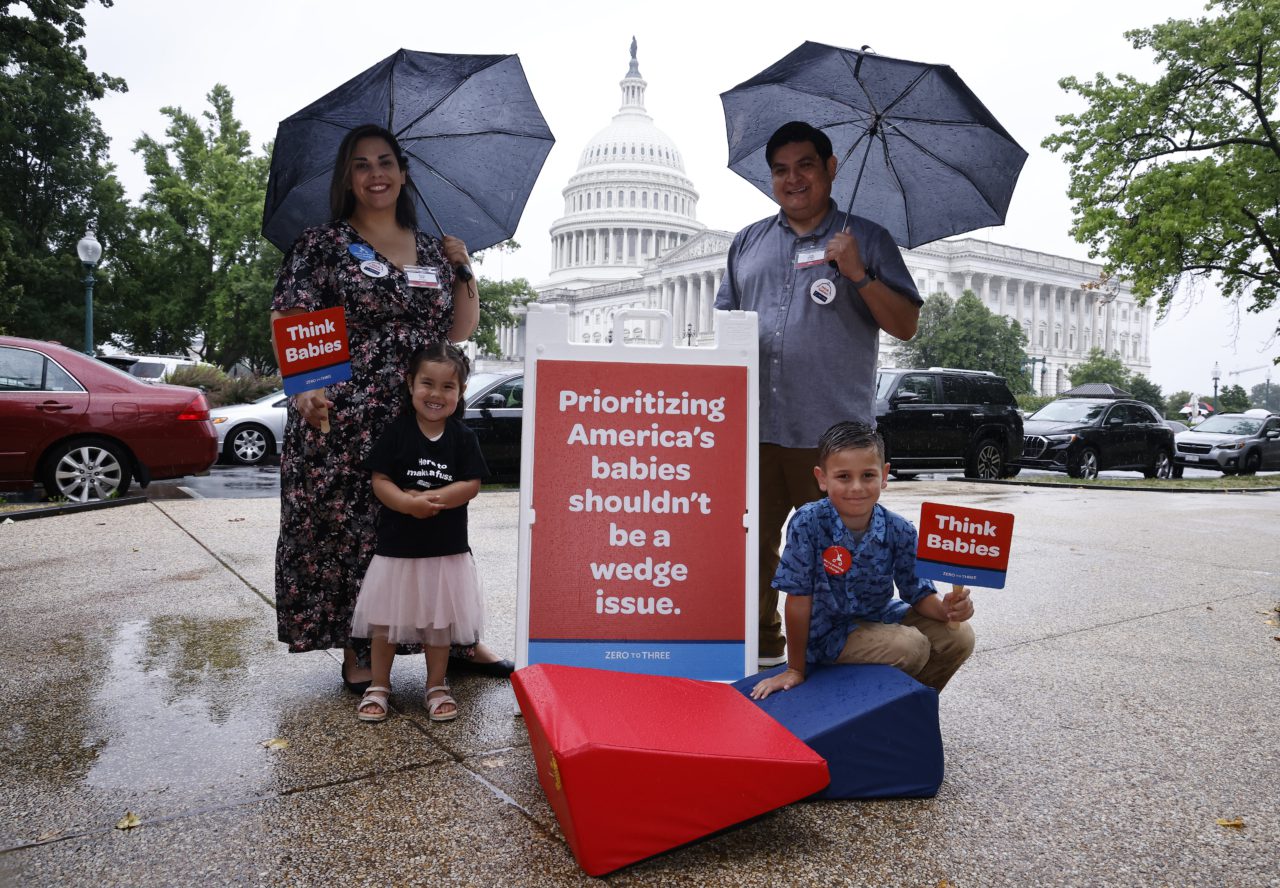 A family poses in front of the U.S. Capitol building with signs saying Think Babies.
