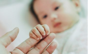 A baby touches an adult's hand.