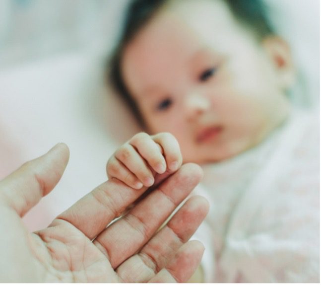 A baby touches an adult's hand.