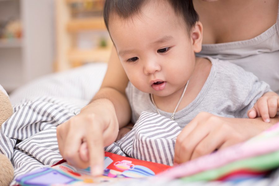 Close up of little baby while the baby learning to reading from mother or looking at the book on the mother's hands (education baby or baby growing up concept) (soft focus)