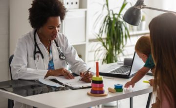 A doctor sits across from a patient holding a baby in the doctor's office.