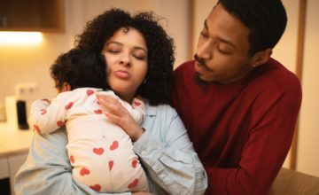 Portrait of young loving multicultural young couple posing with their newborn baby at home, hispanic curly woman holding infant, rubbing little girl back, black husband looking at his wife with child
