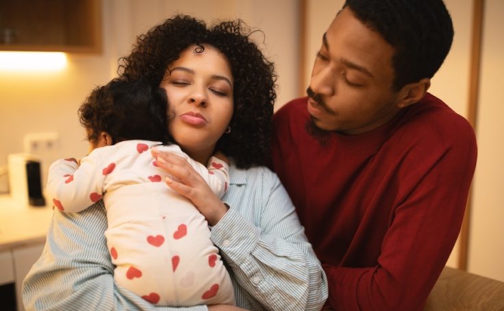 Portrait of young loving multicultural young couple posing with their newborn baby at home, hispanic curly woman holding infant, rubbing little girl back, black husband looking at his wife with child