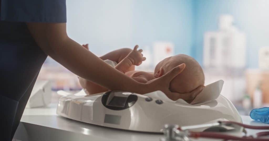 Pediatrician Putting Down a Newborn Infant on Modern Digital Baby Scales in a Maternity Hospital Ward. African Nurse Performing Checks on a Child After Birth in Nursery