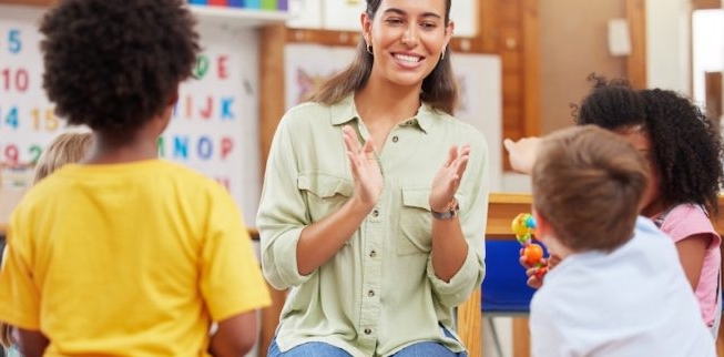 teacher clapping hands in front of four children in classroom
