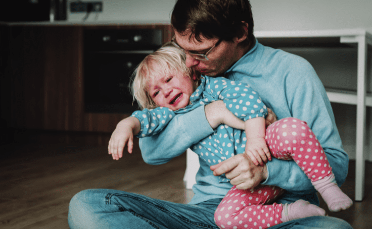 A father comforting a crying and yelling toddler girl.