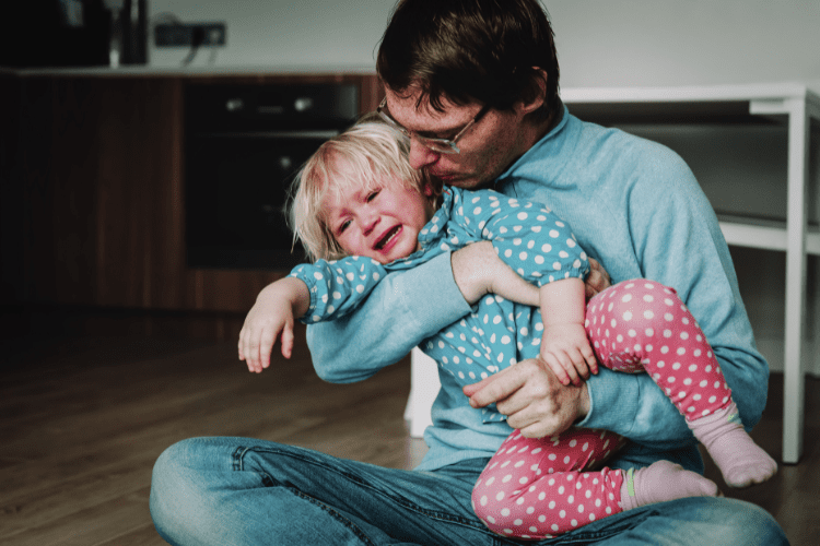 A father comforting a crying and yelling toddler girl.