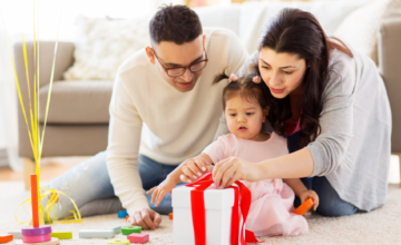 young child opening a gift with her family