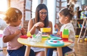 Female caregiver plays with two girls and toy dishes.