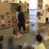 Teacher instructing preschoolers who are seated on a rug.