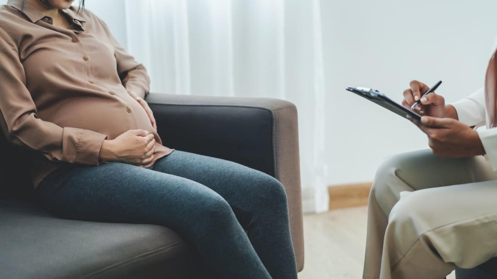 Pregnant woman sits across from her doctor who is taking notes.