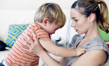 A woman holding an angry toddler calmly talking to him.