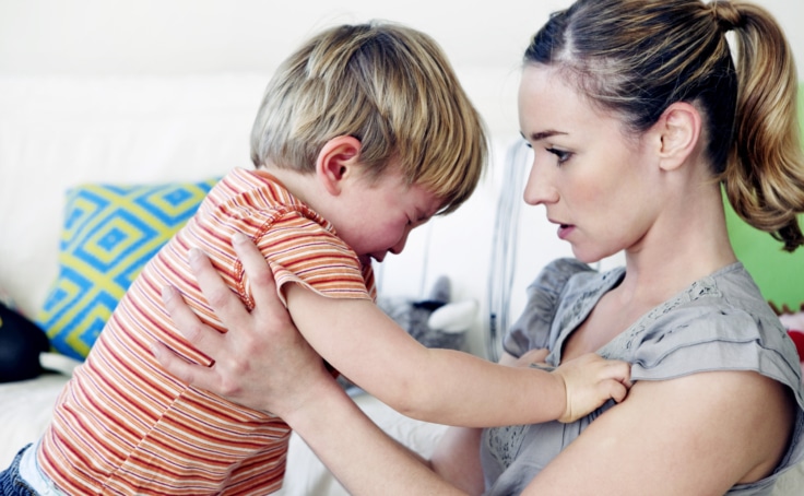 A woman holding an angry toddler calmly talking to him.
