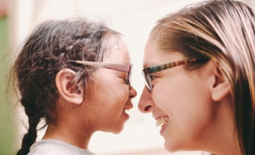 a smiling woman with glasses looks at close range at a female smiling toddler with glasses
