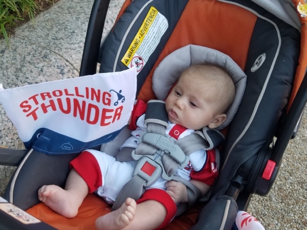 An infant in a stroller with a Strolling Thunder flag