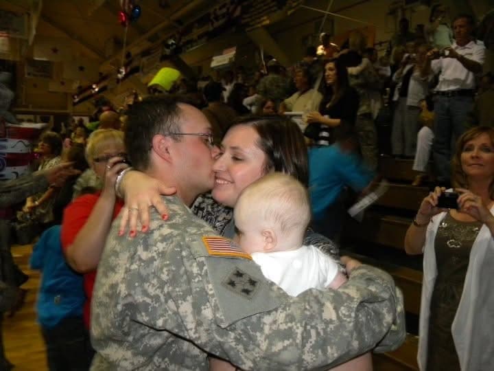 Danielle hugs her husband in his military uniform while holding their baby