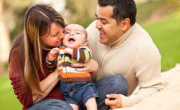 a smiling woman holds an infant while a smiling male lays beside them