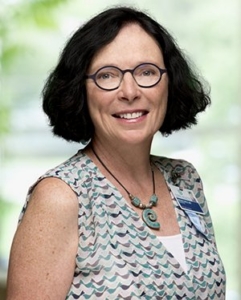a smiling woman with neck-length dark hair wearing glasses and a multi-colored blouse