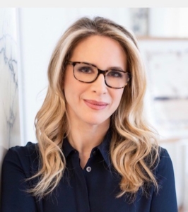 a smiling woman with long blonde hari wearing glasses and a dark blue shirt