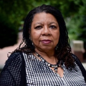 a smiling african american woman with long black curly hair wearing a black and white checkered shirt with black sweater
