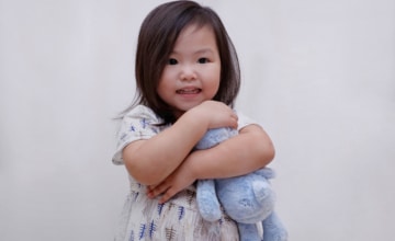 a young female child holds a blue teddy bear