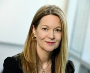 a smiling woman with long blonde hair wearing a black v-neck sweater