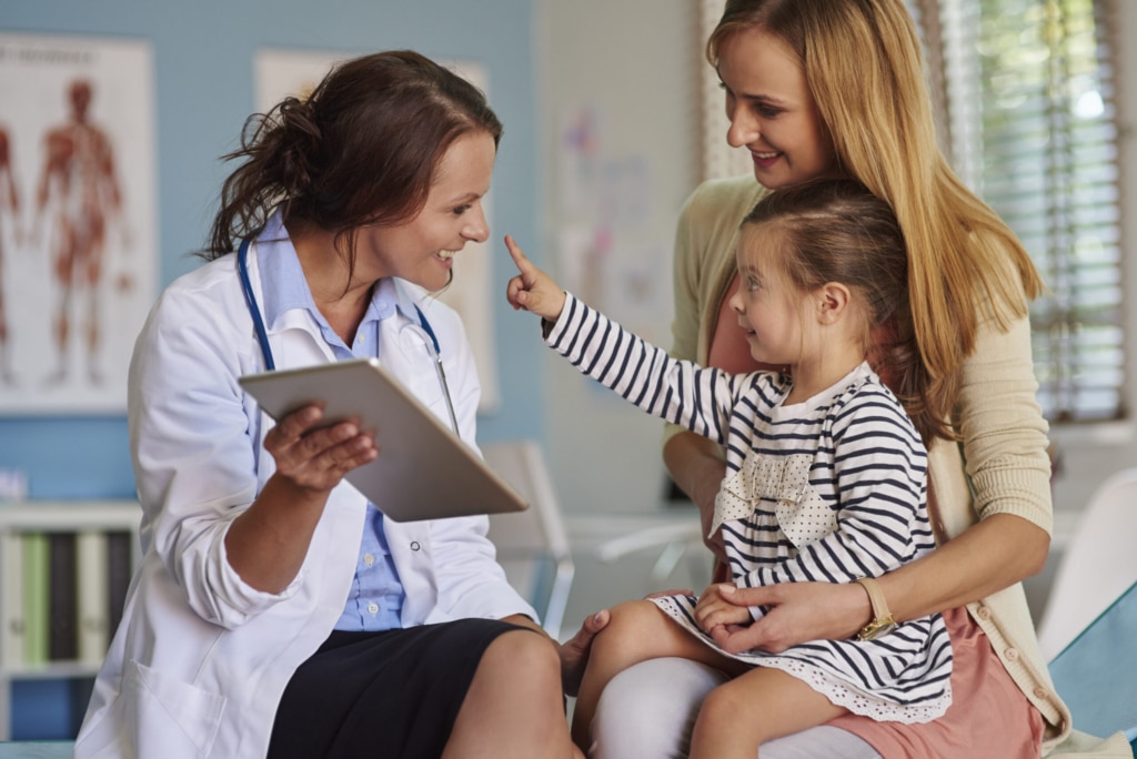 Female medical provider smiling with a toddler and woman in an exam room