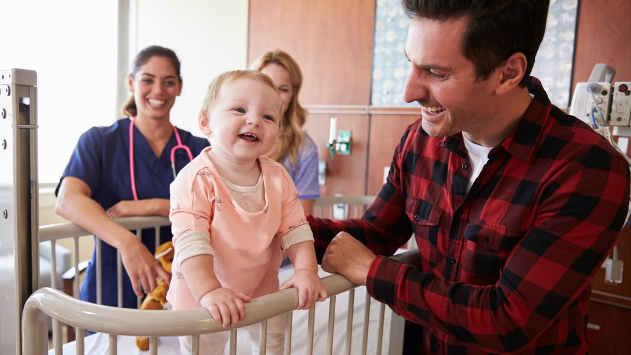 Family in pediatrician's office with baby smiling on a hospital bed