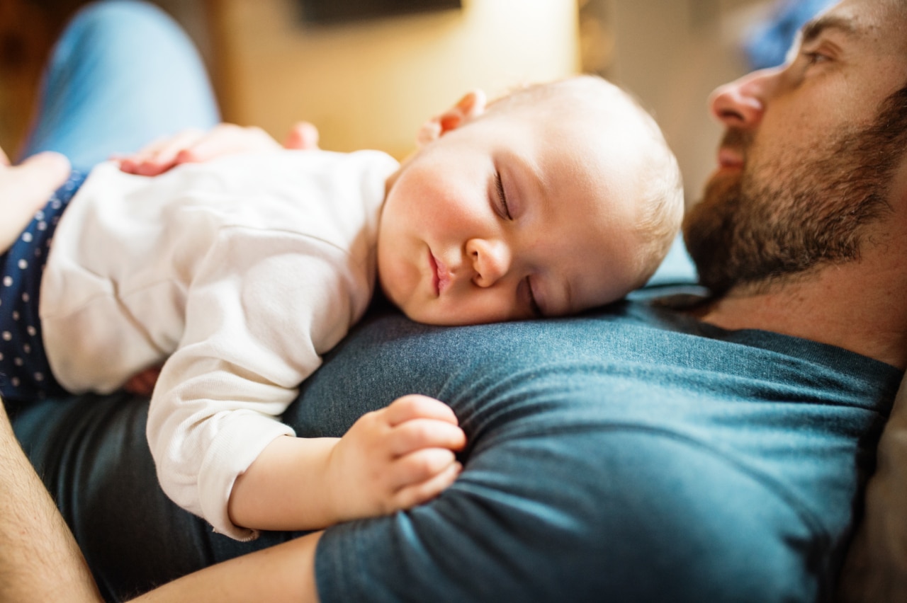 a father is laying down as a baby is sleeping on his chest
