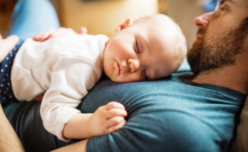 a father is laying down as a baby is sleeping on his chest