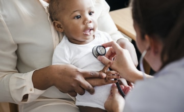 Medical professional holding stethoscope to smiling baby