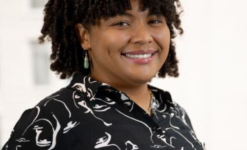 a smiling woman with shoulder-length dark brown curly hair wearing a black and white button up dress shirt